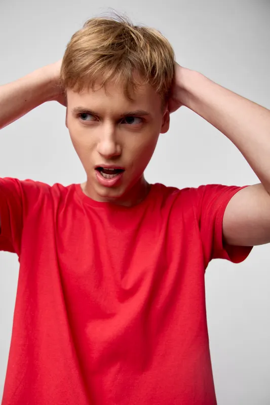 Frustrated boy in a red shirt grips his head, showing confusion and stress, an intense expression and raw emotion captured in a close up, a restless mood and youthful frustration