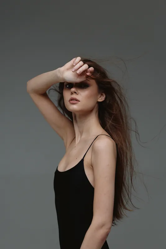 young woman shielding eyes with hand in black tank top with neutral background