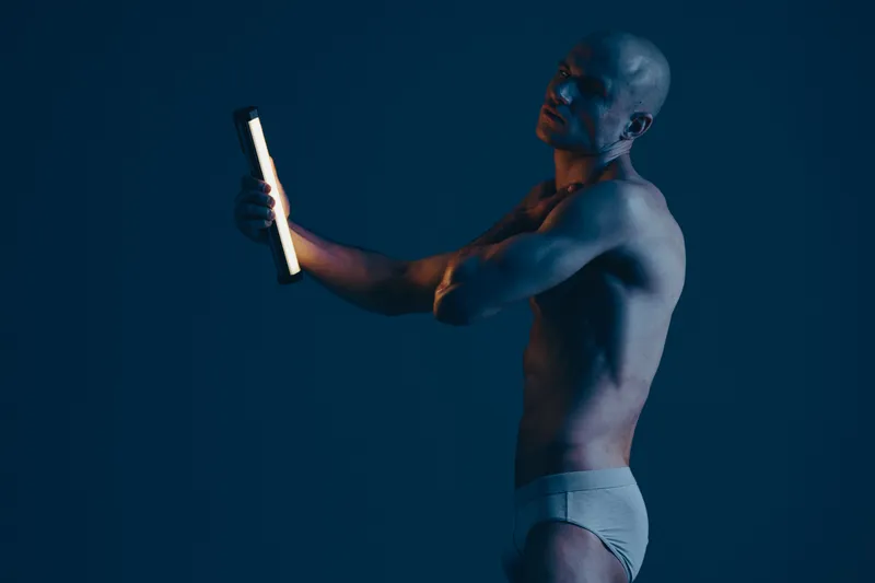 A focused man with a modern aesthetic, illuminated by a light source against a dark background, enhancing the contours of his body. Ideal for artistic concepts.