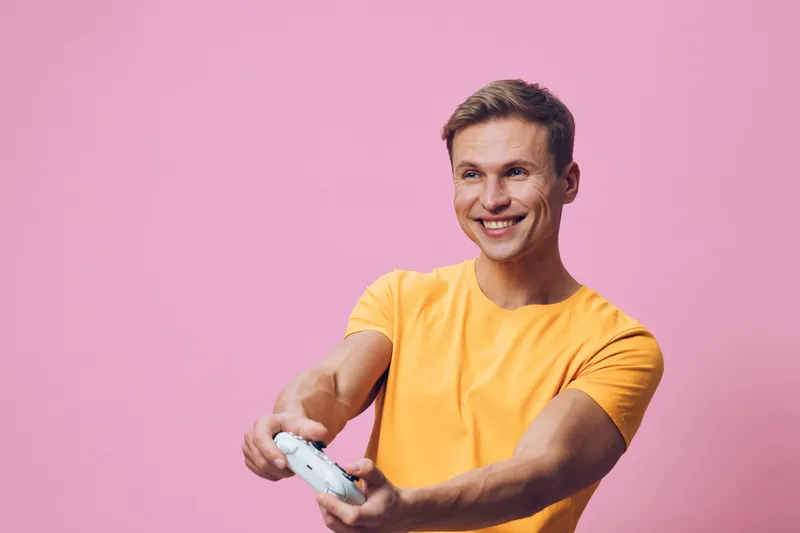 smiling young caucasian man wear yellow t-shirt hold game controller play video game isolated pink background cybersecurity digital detox concept