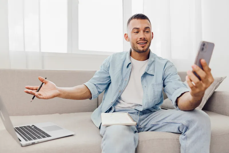 Engaging man using smartphone while sitting on a cozy sofa, showcasing modern lifestyle and technology. Perfect for social media and online connection themes.