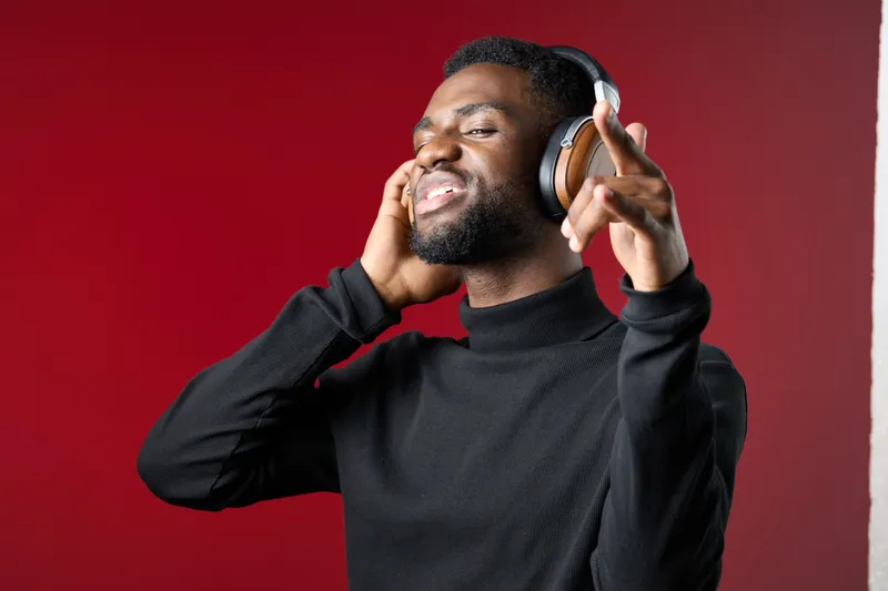 Young Black man enjoying music with headphones against a red background, expressing joy and positivity, perfect for lifestyle and music themes