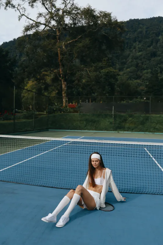 Young female tennis player relaxing on the court, showcasing sporty attire and calm expression amidst a serene green backdrop