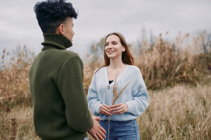 Young couple stands in a windswept meadow sharing a candid moment of genuine connection and honest emotion, captured in natural light with relaxed poses and simple styling for realistic storytelling.