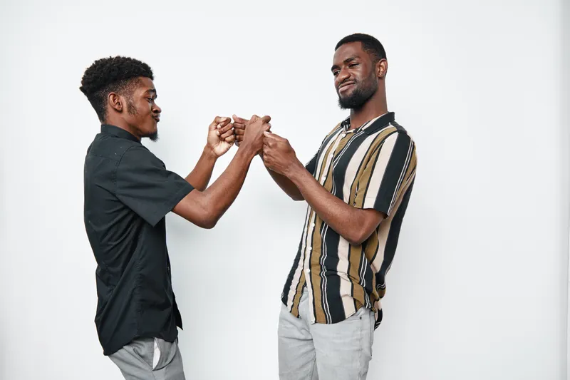 Two black men with dark skin fist bumping and smiling in casual clothes on white background. Friendship, connection, happiness and positive interaction between african american males.