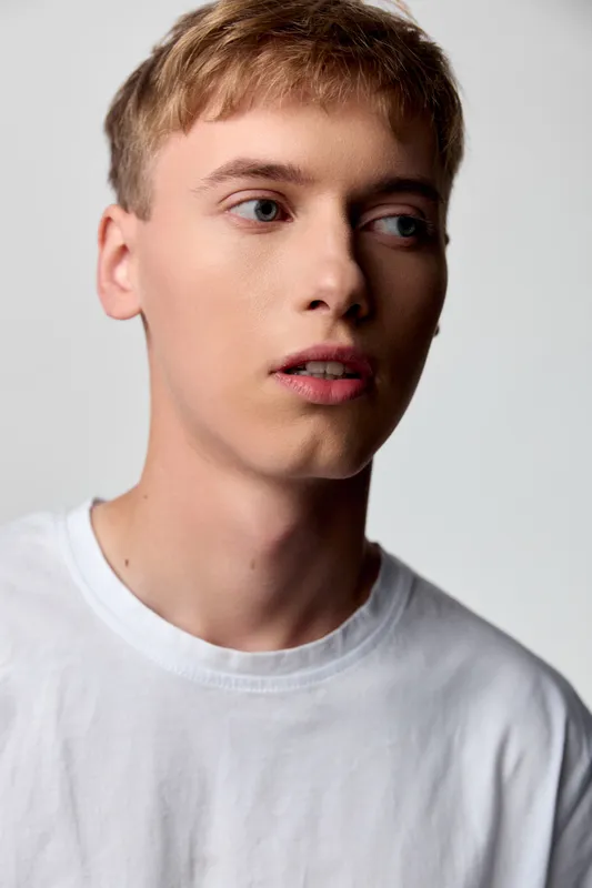 Close up of a young man in a white tee, soft studio lighting, thoughtful expression, clean casual style, neutral backdrop, modern fashion mood and natural skin tone detail