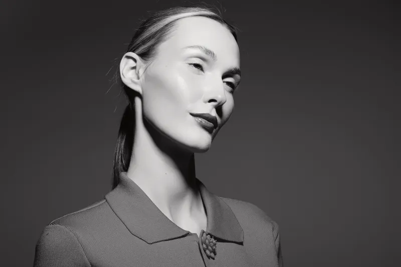 Elegant Caucasian woman with pale skin poses in black and white studio portrait wearing a textured jacket with a brooch and sleek hairstyle. Concept of fashion and beauty.