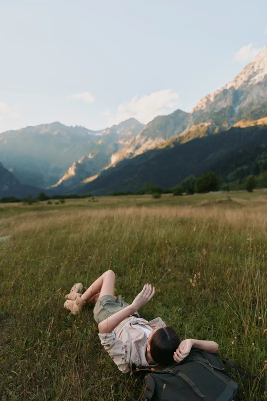 Young woman with short hair lies on grass in a mountain meadow enjoying a peaceful moment during a sunny day.