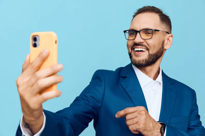 A professional man in a blue suit takes a selfie against a solid color background, projecting confidence, optimism, and focus in a modern corporate environment.