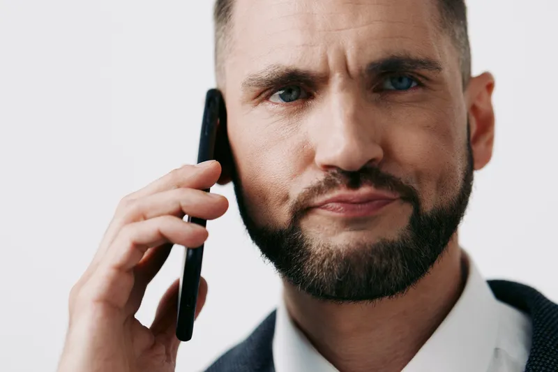 A professional business man on a solid color background, exuding confidence and focus while speaking on a mobile phone during a workday moment, ready for discussion.