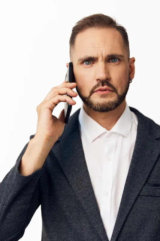 A focused business professional man stands against a colored isolated background, showing confidence and determination while speaking on a call.