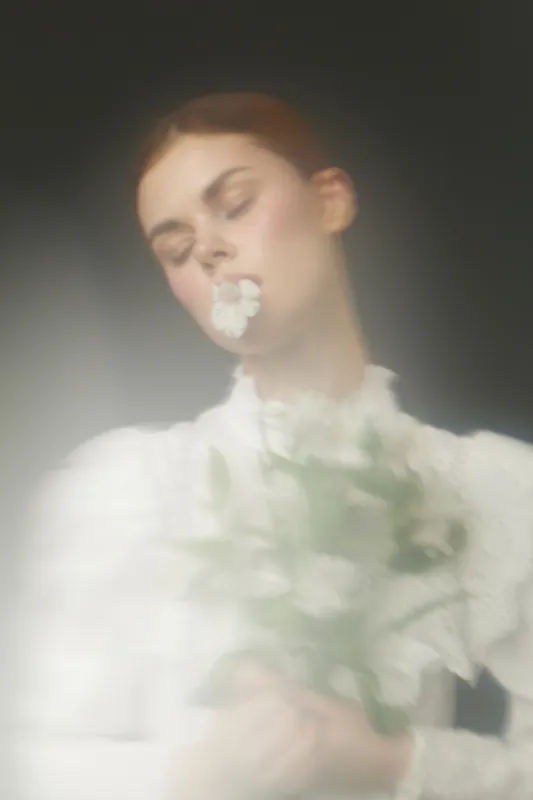 Soft focus portrait of a serene woman holding white flowers, in a delicate, vintage blouse, showcasing emotions of tranquility and grace