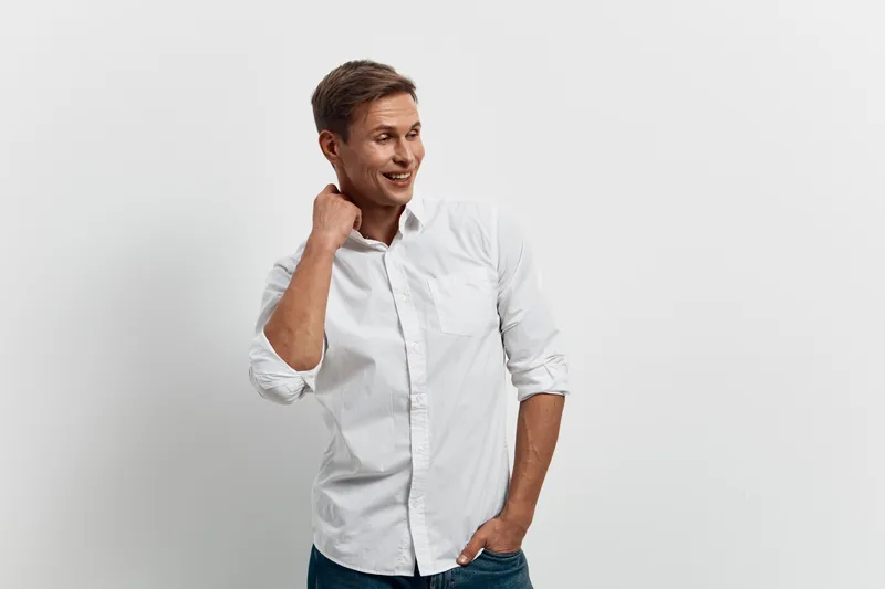 Smiling happy young caucasian man wear white shirt look aside thoughtful hold hand near neck isolated on white background mental health gadgets concept