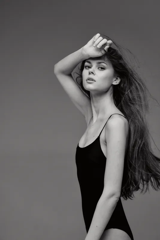 Black and white portrait of a young woman with long hair wearing a black sleeveless outfit posing thoughtfully.