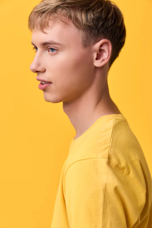 Profile of a youth male in a yellow shirt against a bright studio backdrop, clean lines, warm lighting, contemporary fashion vibe, confident and calm expression