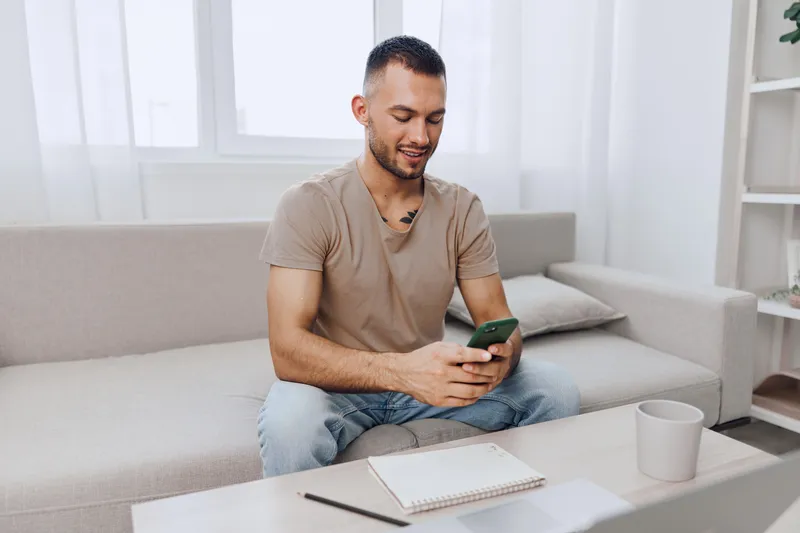 Engaged man using a smartphone while sitting on a comfortable sofa in a bright, modern living space. Innovation and technology blend seamlessly in this lifestyle scene.
