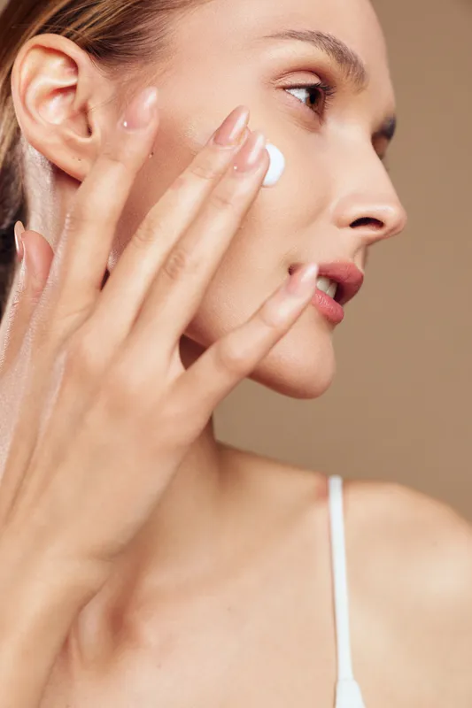 Woman skincare face cream lotion beauty spa close up portrait, young female applying facial moisturizer with fingers, profile view, smooth glowing skin, self care routine