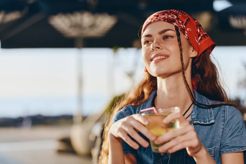 lifestyle woman in modern boho-western denim street style enjoying a sunny day with a refreshing drink, film color warm tones and relaxed mood