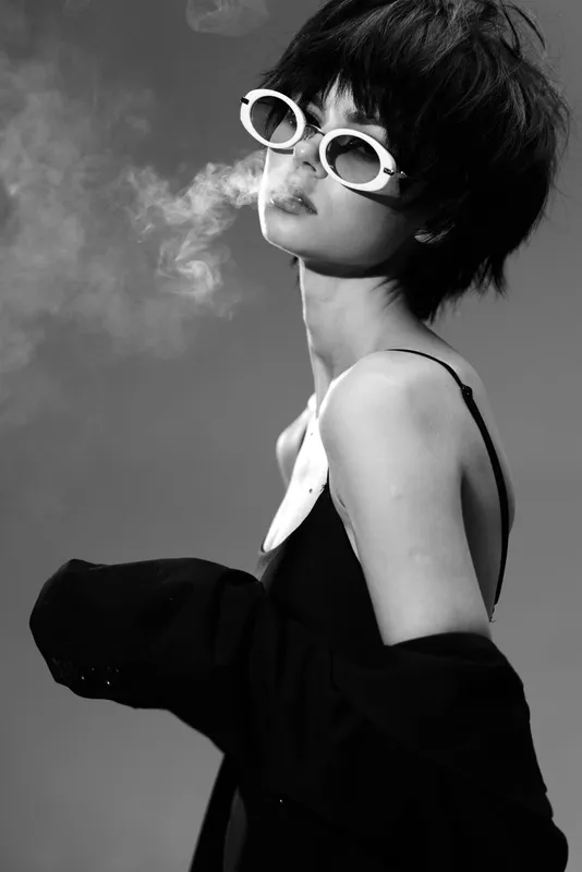 Black and white portrait of a stylish woman wearing sunglasses with smoke in background, modern fashion, edgy mood.