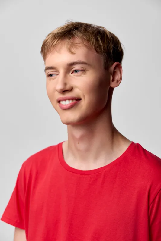 Smiling man in a red shirt stands against a light background, conveying casual style, relaxed mood, and approachable confidence for lifestyle, fashion and everyday wear.