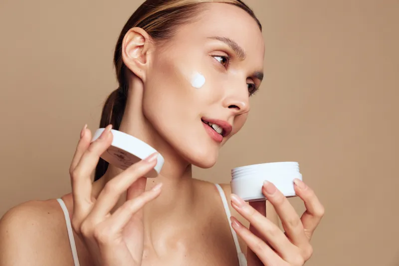 Young woman applying face cream, close up on warm brown background, self care and skincare concept, soft studio lighting, wellness mood, healthy skin, routine