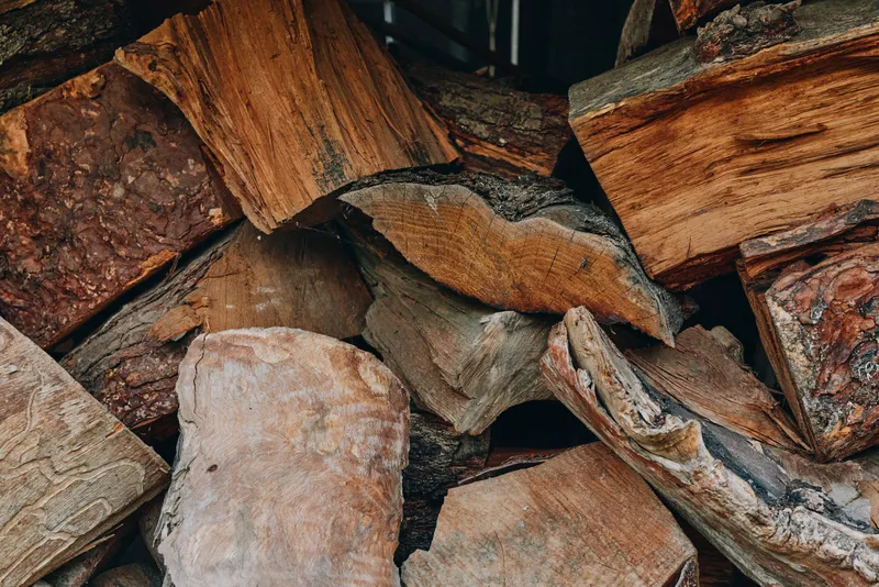 Firewood logs stacked in a rustic woodpile, split wood with textured bark and timber grain, closeup of chopped pieces for fireplace, heating and outdoor storage.
