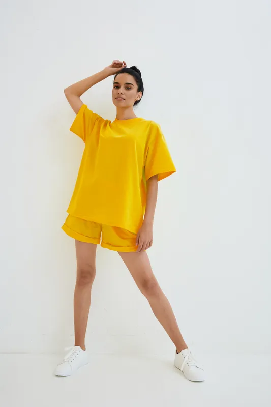 woman in bright yellow casual outfit posing relaxed indoors, minimalistic white background, comfortable summer clothing style, sporty and modern vibe