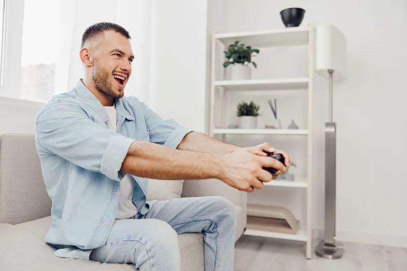 Excited man playing video games at home, enjoying his leisure time with vibrant colors and a modern setting, surrounded by plants and stylish decor.