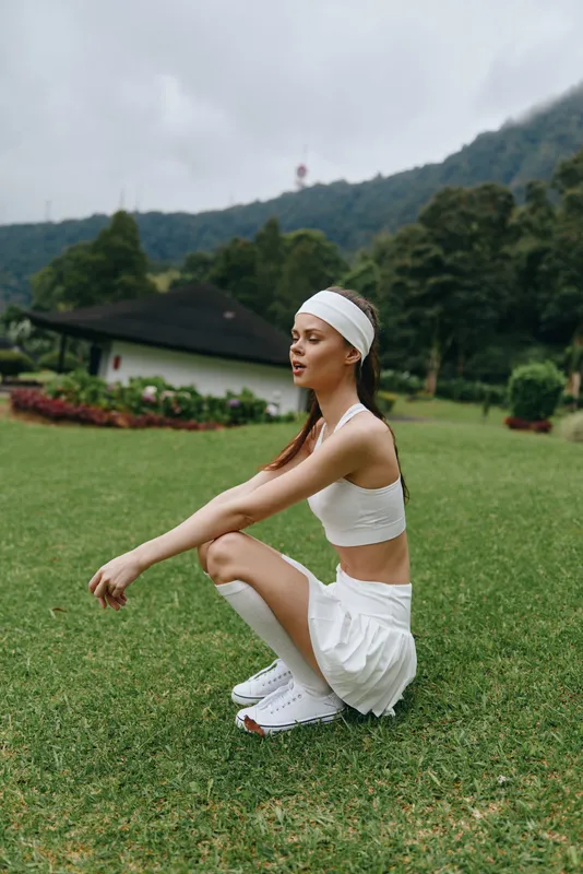 A young athletic woman wearing a sports bra and skirt, practicing yoga outdoors on a green lawn, embodying health, fitness, and serenity in a natural setting