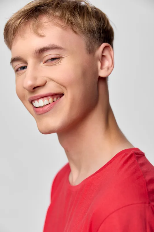 Smiling young man in a red shirt with a bright, friendly expression, close-up shot highlighting a cheerful smile and warm mood, ideal for lifestyle branding and social media campaigns