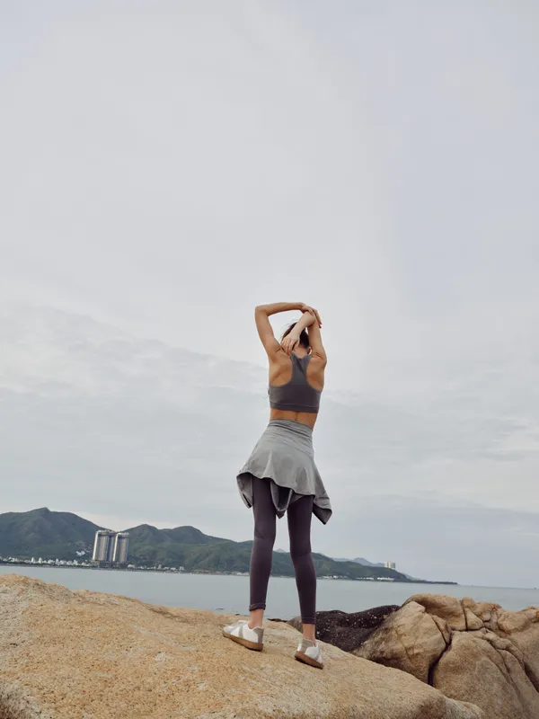 Young fit woman stretching outdoors in activewear, enjoying the serene coastal view and embracing a healthy lifestyle while preparing for a workout session
