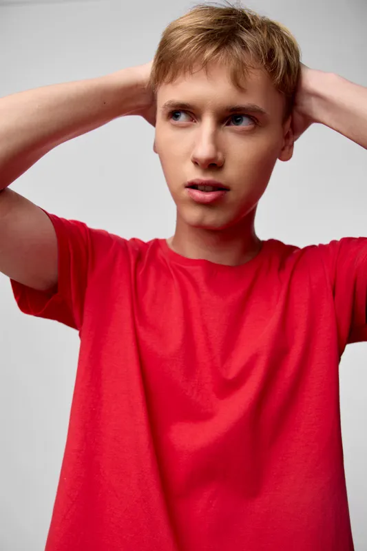 Confused child with a puzzled expression touching his head, wearing a bright red shirt captured in a studio setting with soft lighting conveying thought, stress and introspection