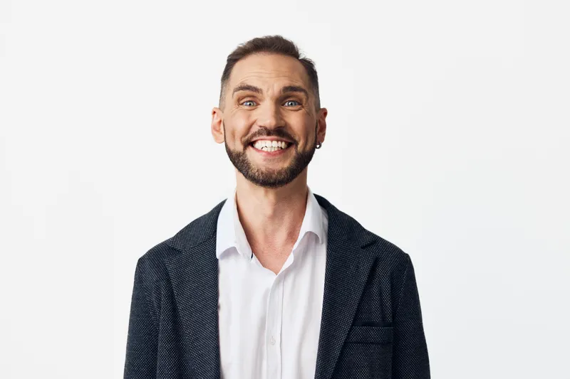 A professional man in business attire stands against an isolated white background, exuding confidence and calm. His broad smile conveys approachability, leadership, and readiness for strategic
