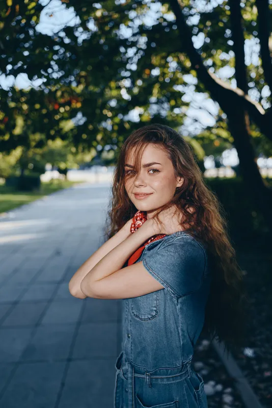 lifestyle woman in modern boho-western denim street style standing outdoors with natural greenery, film color tones, soft sunlight, and relaxed confident expression