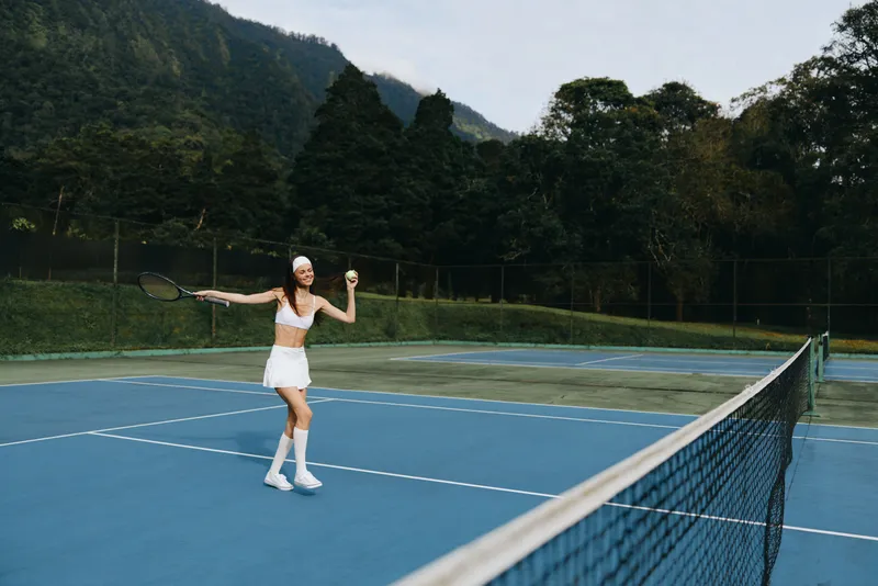 Young female tennis player celebrating on the court, wearing a sporty outfit, showcasing joy and energy in a vibrant outdoor setting with a lush green background
