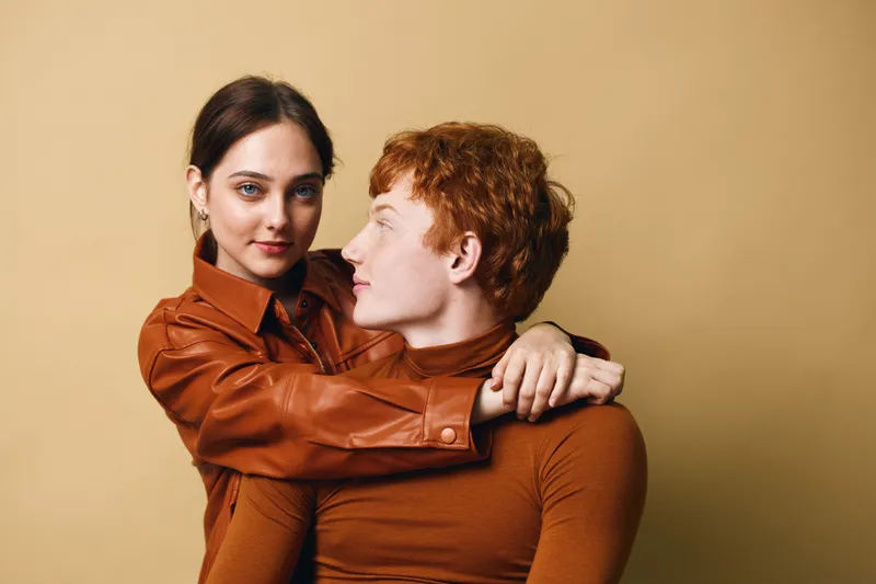 Couple embracing and looking at each other with affection in studio, woman and man wearing brown outfits posing on beige background for portrait photography.