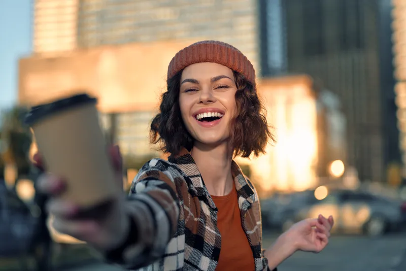 woman smile coffee city candid urban portrait happiness as she offers a takeaway cup in golden hour glow, authenticity and candid lifestyle captured with emotional storytelling and joy