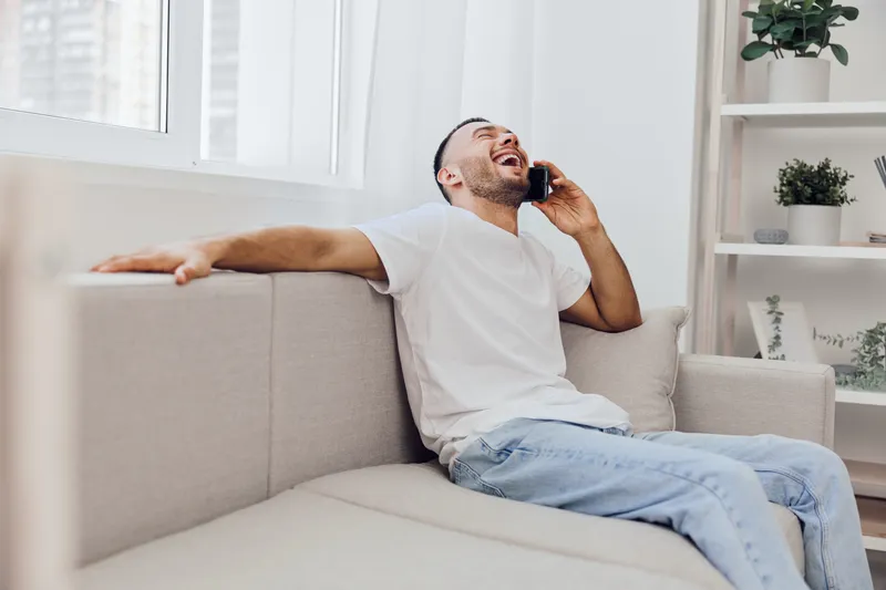 Laughing man on the phone, showcasing emotional vulnerability and genuine connection in a cozy living space, ideal for themes of mental health and authenticity.