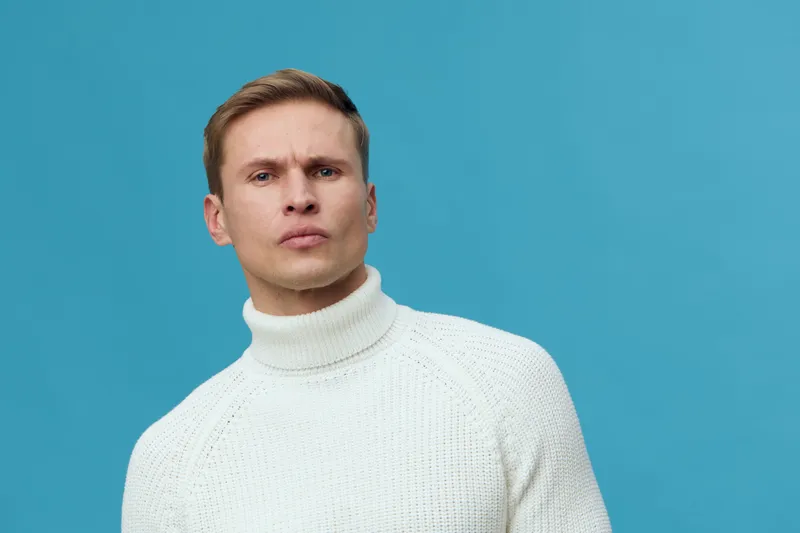 serious man wearing white turtleneck sweater blue background front view focused confident expression portrait mental health concept