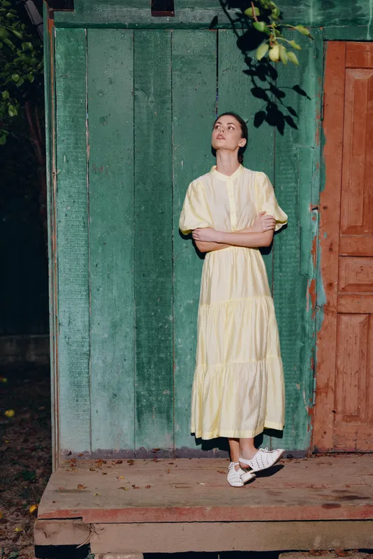 Woman in yellow dress on rustic porch by green door looking up with authenticity inclusivity, light summer scene