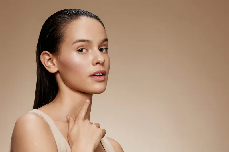 Young model with glowing skin and wet hair showcases beauty, elegance, and confidence against a soft beige background, emphasizing self care and skincare routines