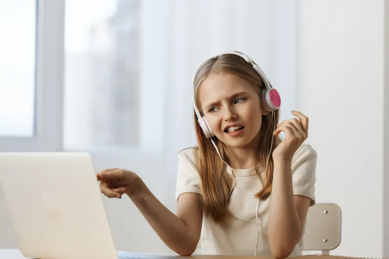 Cheerful girl with headphones engaged in online learning or music, enjoying her time in a bright room with natural light