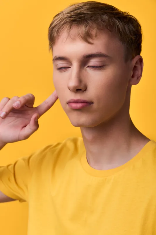 Calm, meditation and focus with a serene quiet mood. An individual with eyes closed and finger to temple, wearing a yellow shirt against a vibrant backdrop, conveying inner balance and mindful