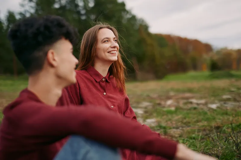 A candid outdoor portrait of a young couple sitting in an autumn field, focused on natural smiles and authentic interaction that conveys honesty, authenticity and easygoing charm.