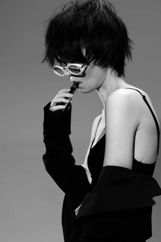 Black and white portrait of a stylish woman wearing sunglasses and dark clothing with short hair.
