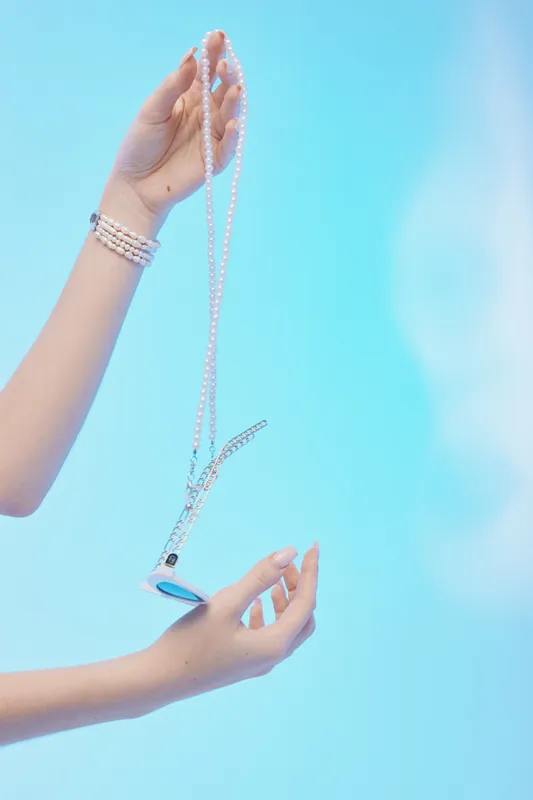 Woman hands holding a pearl necklace with pendant against blue background. Concept of beauty, fashion, elegance, jewelry, and luxury accessories in a minimalist style.