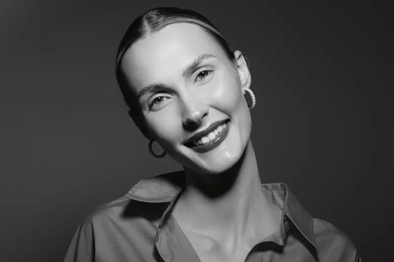 Smiling white woman with pale skin and earrings poses in studio wearing an open collar shirt. Concept of beauty, happiness, fashion, and female portrait.
