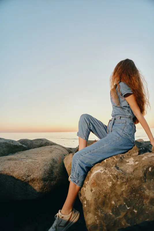 lifestyle woman in modern boho-western denim street style sitting on rocks during sunset with natural light and film color effect