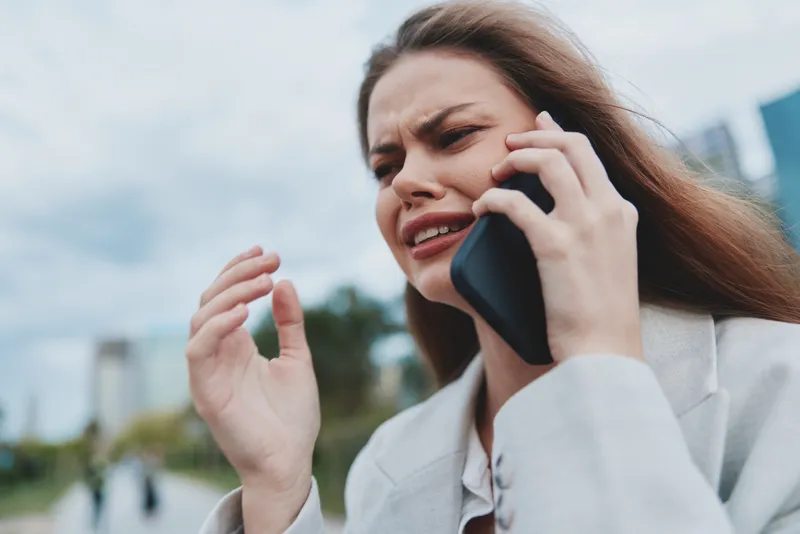 upset woman talking on phone showing stress and anxiety in outdoor urban setting with blurred city background and casual jacket