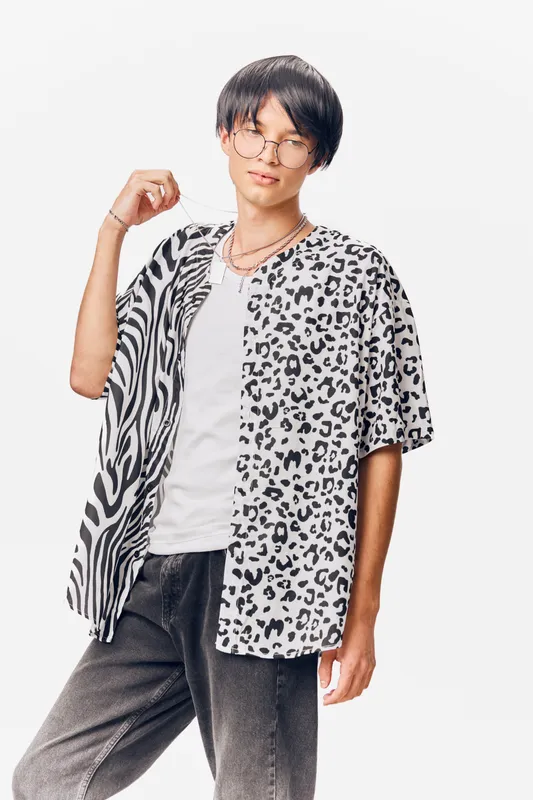 young man wearing round glasses and trendy animal print shirt posing against white background, casual style with confident expression and relaxed posture